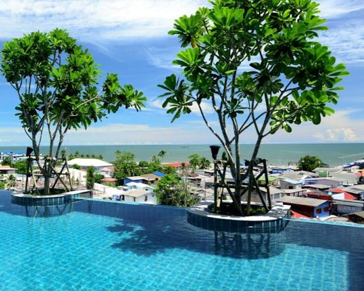 Rooftop infinity swimming pool at Hisea Hua Hin Hotel featuring decorative trees and a panoramic view of the Hua Hin cityscape and the Gulf of Thailand.