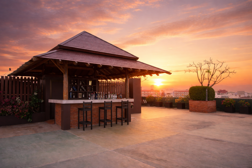 Panoramic view of Hisea Huahin Hotel's rooftop terrace with sun loungers and a central bar pavilion during a dramatic sunset.