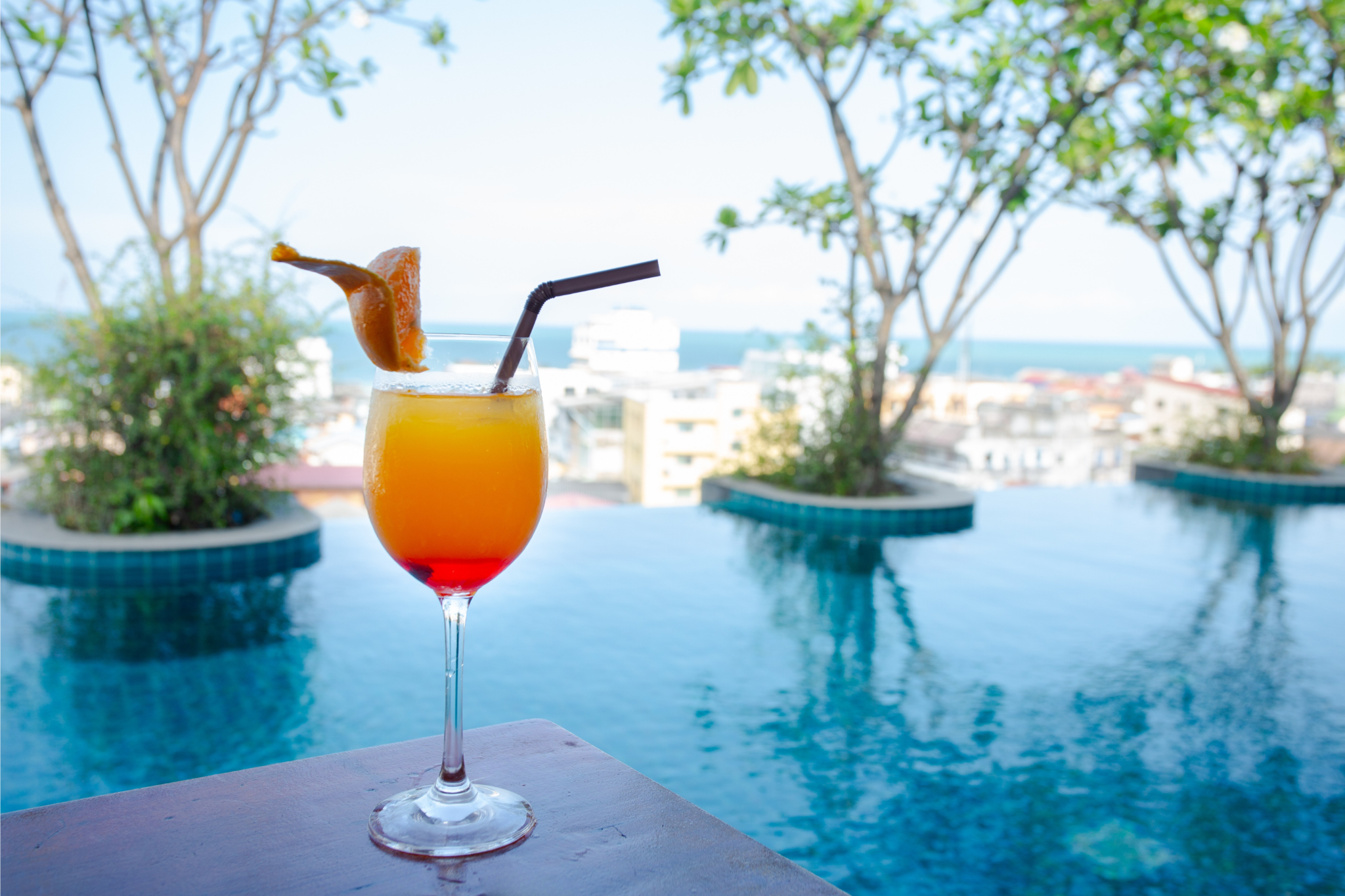 infinity pool at Hisea Hua Hin Hotel with a tropical sunset cocktail and panoramic city views.